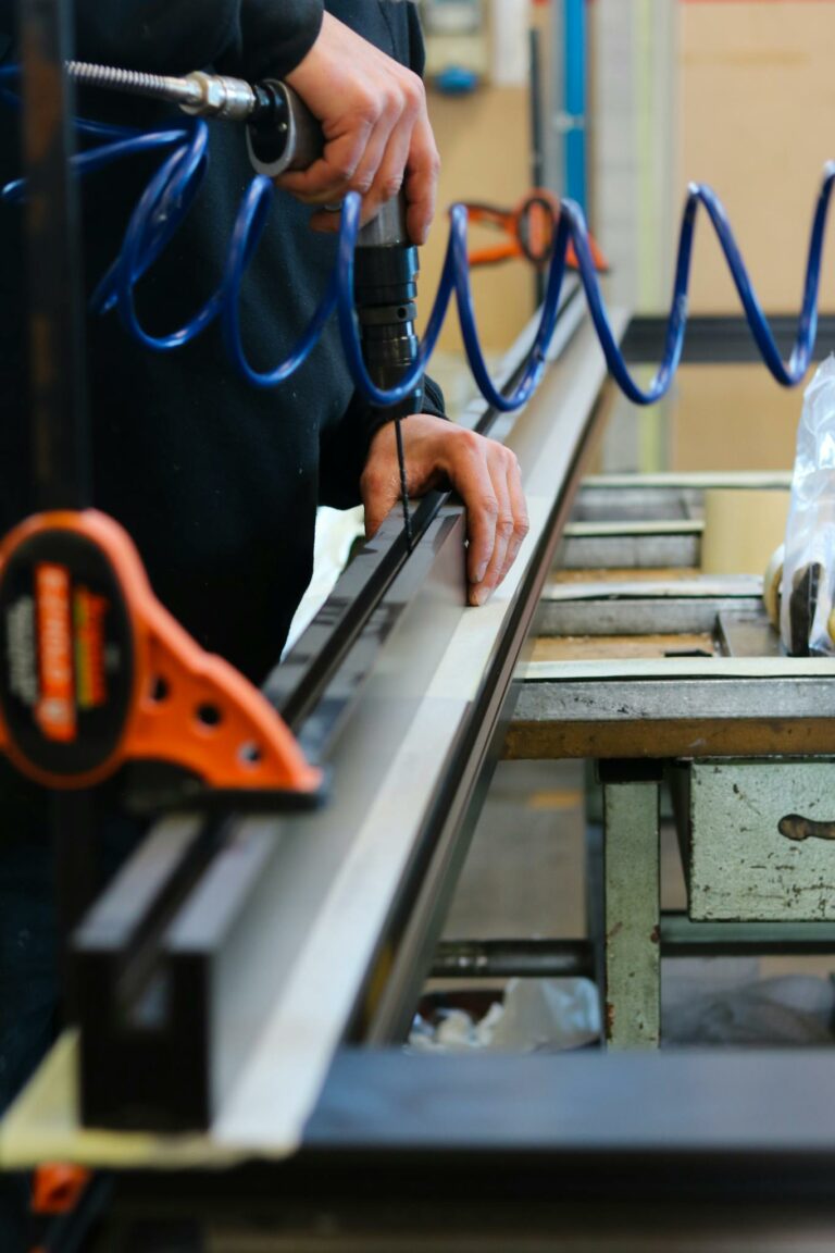 A worker carefully drills metal with precision in an industrial workspace, focusing on craftsmanship.