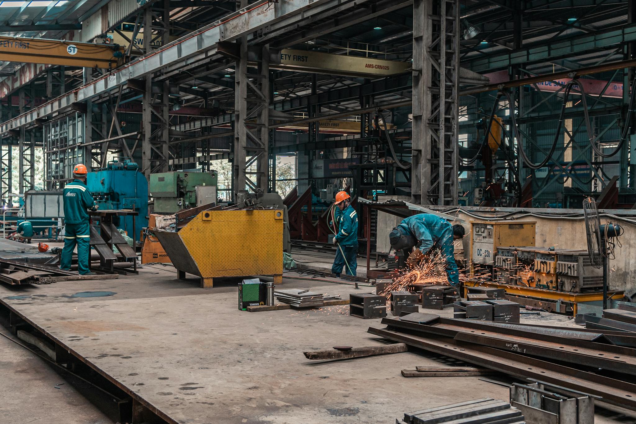 Workers in a metal workshop engaged in active construction and welding tasks.