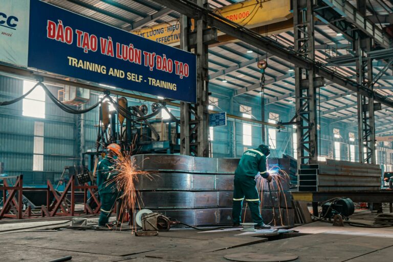 Workers weld metal structures in a bustling industrial factory, showcasing a dynamic work environment.
